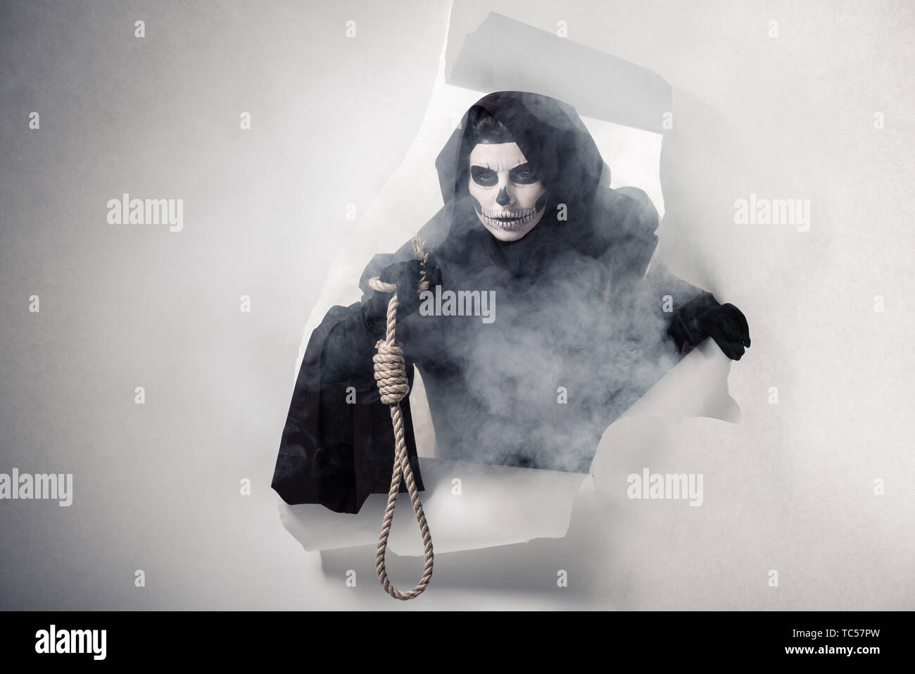 woman in death costume holding hanging noose and getting out of hole in paper Stock Photo