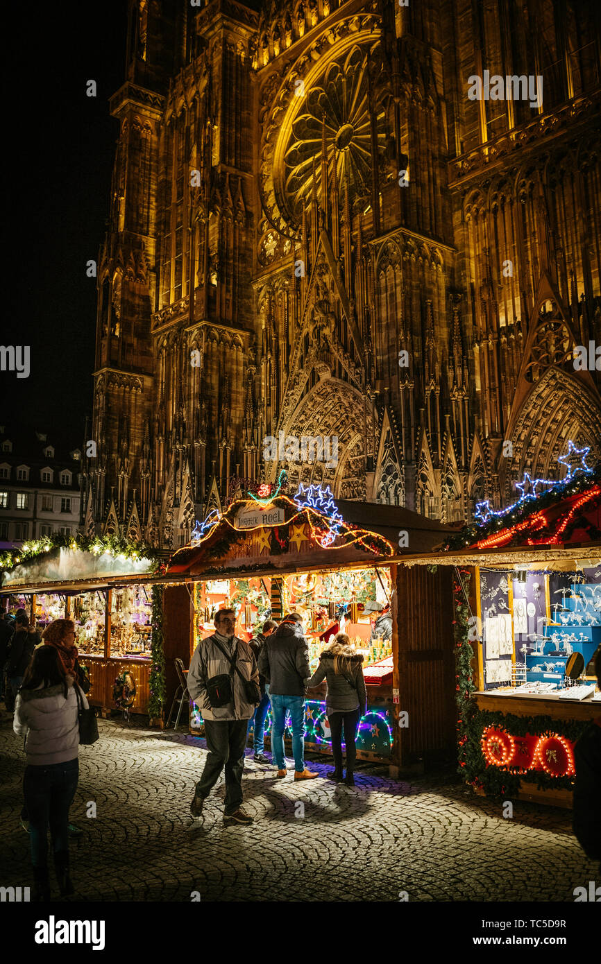 STRASBOURG, FRANCE - NOV 29, 2017: Customers admiring the toys, souvenirs and toys in central chalet of the Strasbourg Christmas market with Notre-Dame cathedral in the background Joyeux Noel Stock Photo