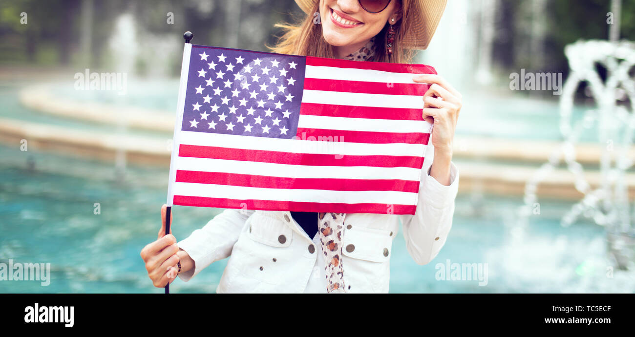 Happy young patriot woman in hat stretching USA flag in park concept, 4th of July, Indendence day Stock Photo