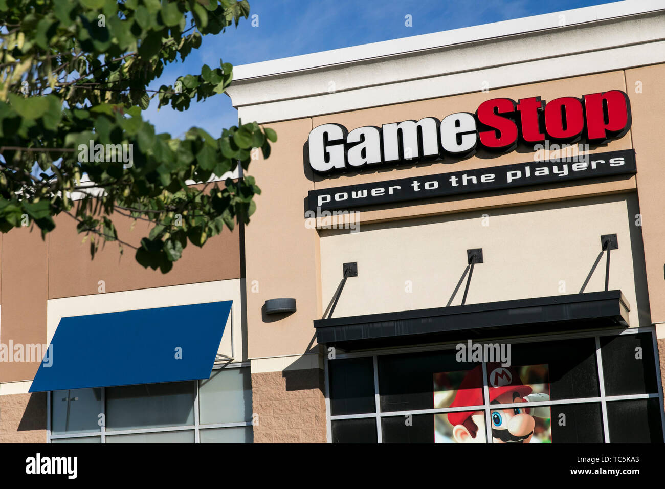 A logo sign outside of a GameStop retail store location in Martinsburg