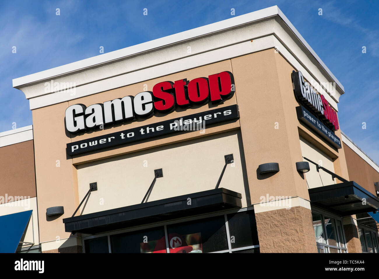 A logo sign outside of a GameStop retail store location in Martinsburg