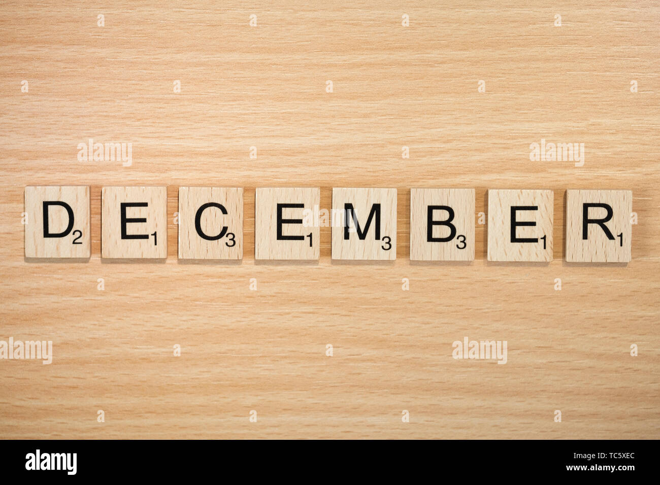 The word December, spelt out using wooden tiles on a wood effect background with scrabble numbered score values. Stock Photo