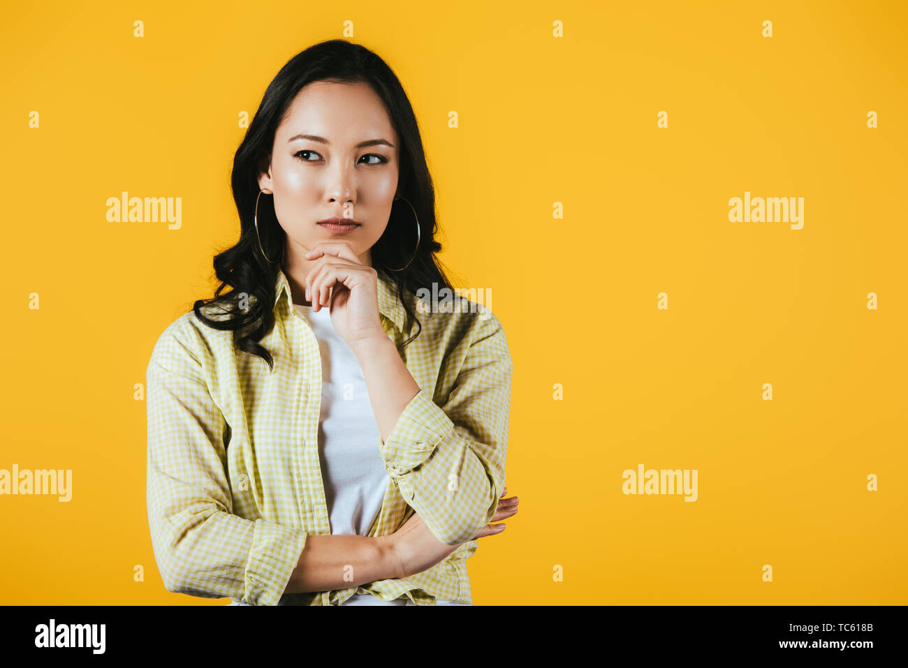 pensive brunette asian girl isolated on yellow Stock Photo