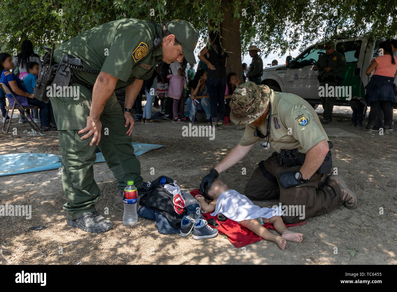 U.S. Fish and Wildlife Service Officers assist with medical aid for an infant after a group of illegal migrants from central America that crossed the Rio Grande River May 31, 2019 near McAllen, Texas. The faces are obscured by the Border Patrol to protect their identity. Stock Photo