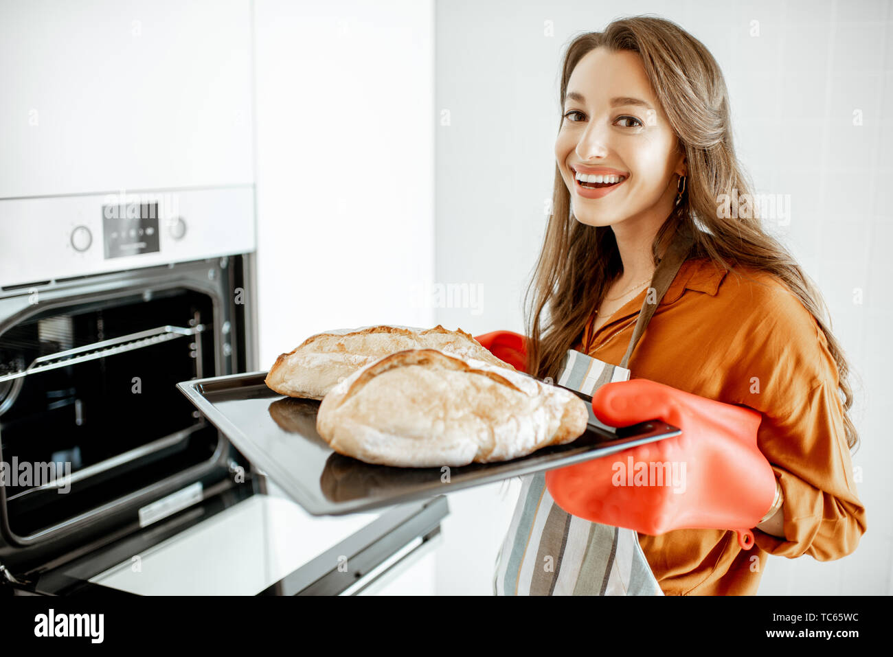 Portrait of a beautiful young woman baking bread in the oven at the modern white kitchen at home Stock Photo