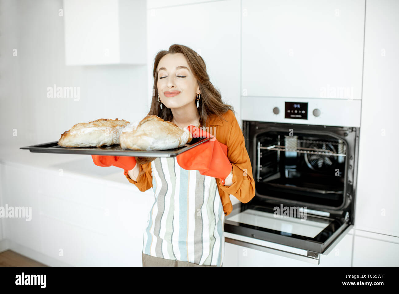 Portrait of a beautiful young woman baking bread in the oven at the modern white kitchen at home Stock Photo