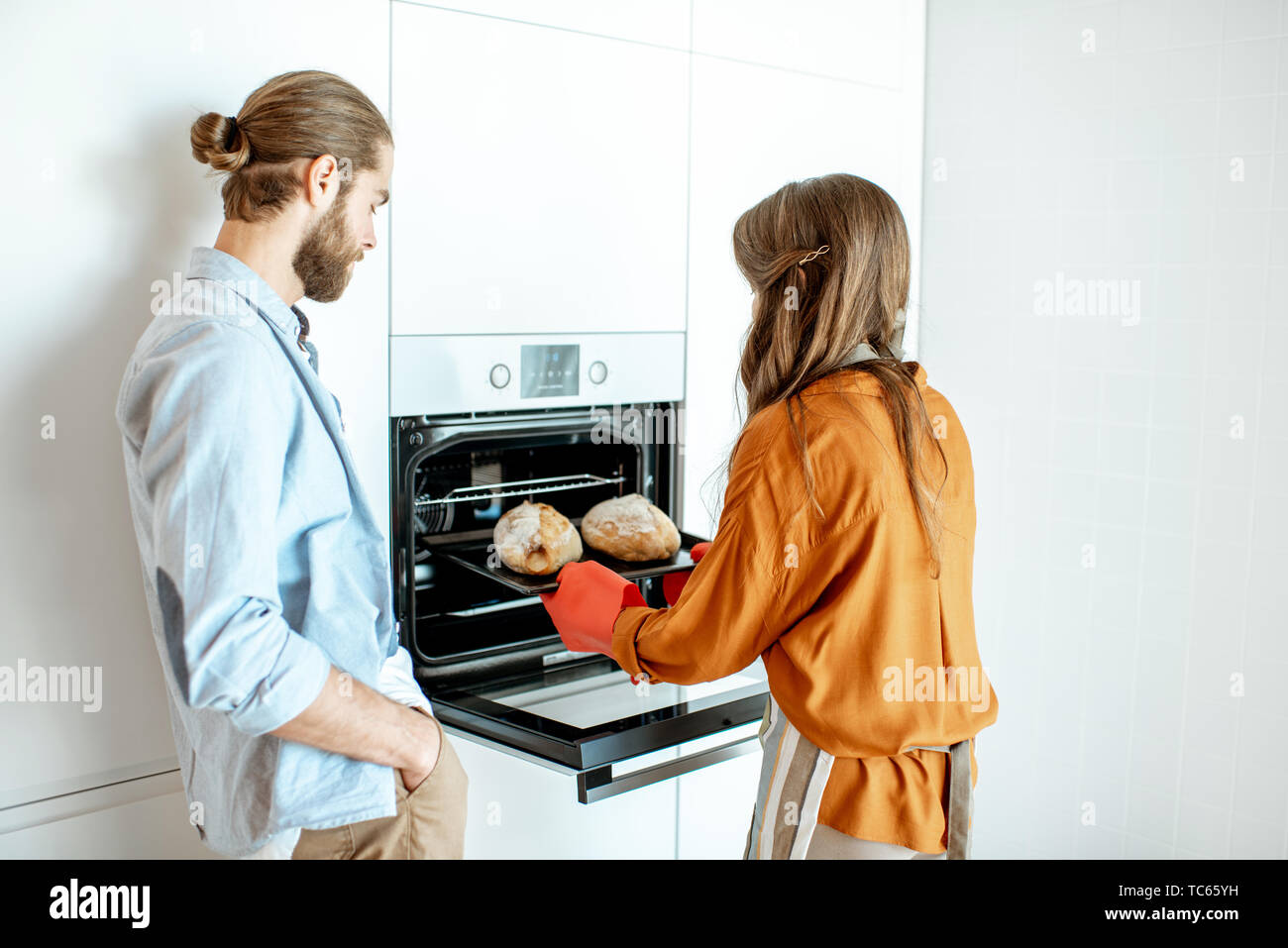 Young and cheerful couple baking breads at the modern white kitchen at home Stock Photo
