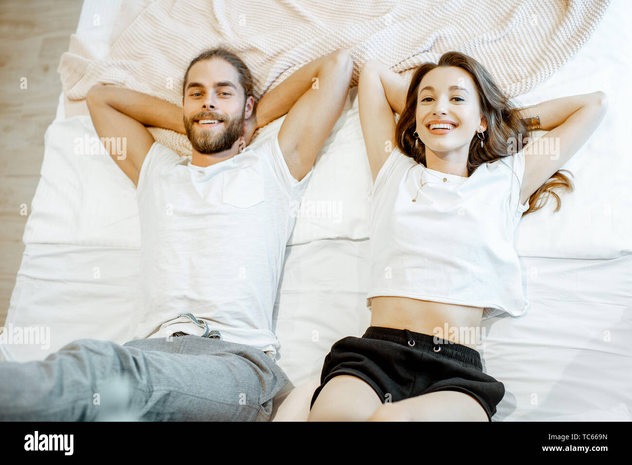 Portrait of a young and cheerful couple lying on the bed, view from