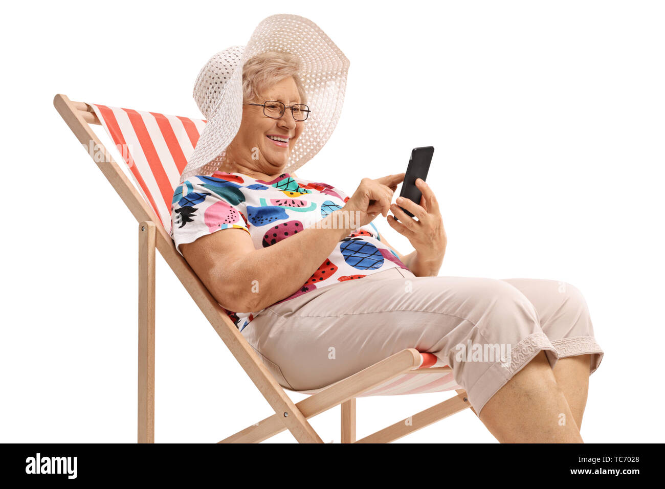 Senior woman sitting in a deck chair and looking at a phone isolated on white background Stock Photo