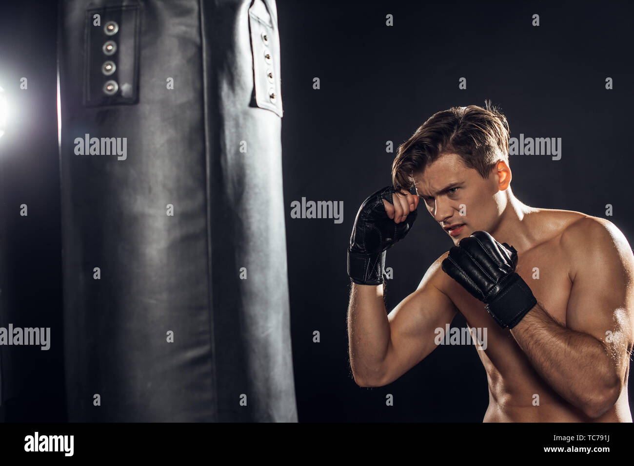 Tired boxer in gloves training with punching bag on black Stock Photo