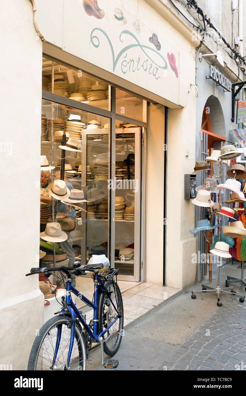 Stacks of hats, Panamas and trilbys with jolly hat stand and blue bicycle in a cobbled side street in the old quarter of L'Isle-sur-la-Sorgue, Stock Photo