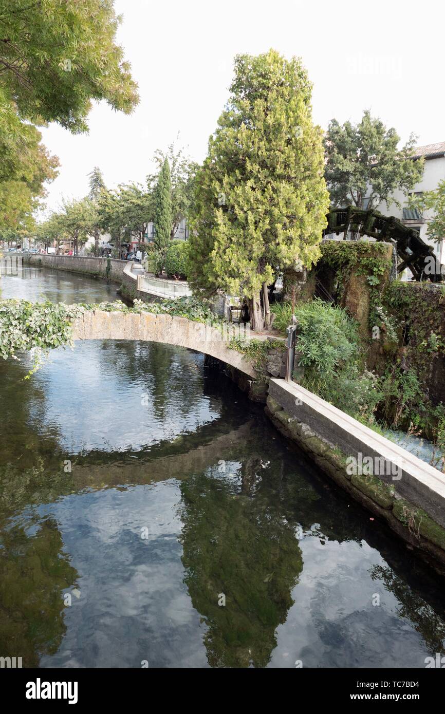 Crystal clear waters of the River Sorgue reflect a bridge, water wheel and over hanging trees in the historic town of L'Isle sur la Sorgue, Provence, Stock Photo