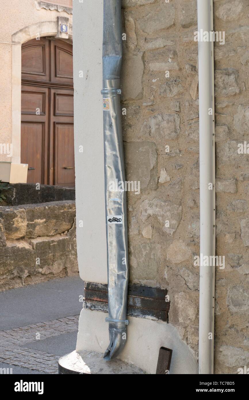 Battered aluminium drainpipe on a precarious street corner, reinforced with metal bands, opposite a handsome, period, wooden panelled door in L'Isle Stock Photo
