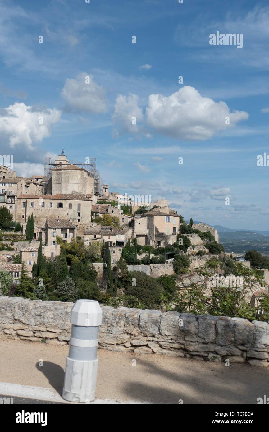 Sky blue day with puffy white clouds and long shadows, tumbling down the hillside past the historic mountain town of Gordes in the Vaucluse, Stock Photo