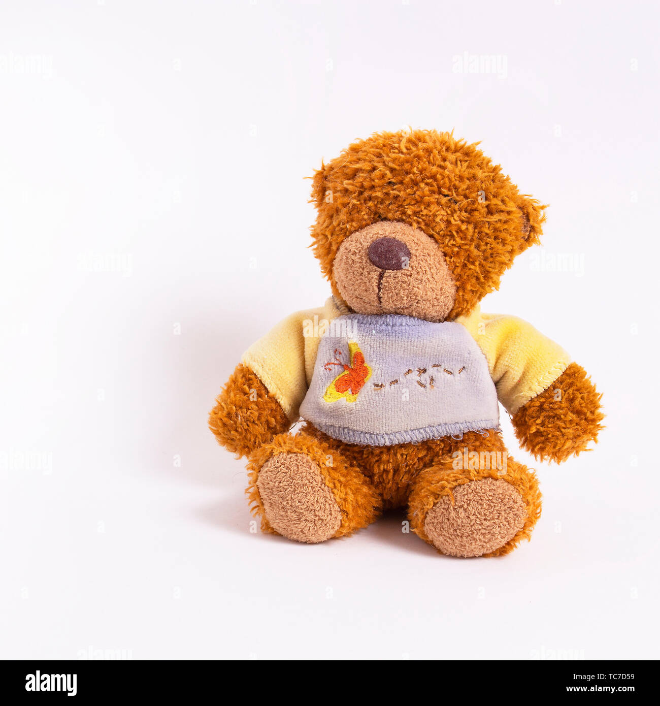 A small teddy bear in a yellow-blue sweater sits on a white background. Children's soft toy. Happy childhood Stock Photo