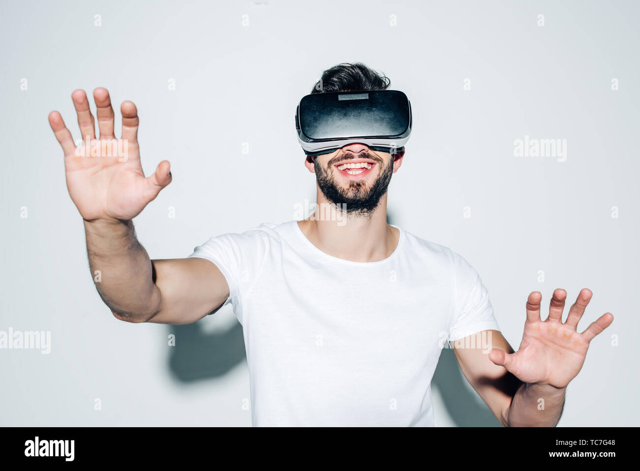 cheerful bearded man wearing virtual reality headset while gesturing on white Stock Photo