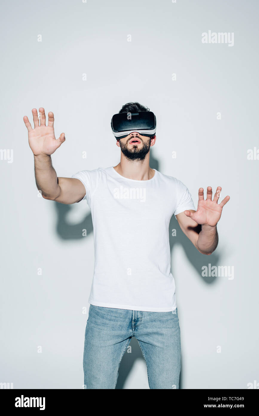 surprised bearded man wearing virtual reality headset while gesturing on white Stock Photo