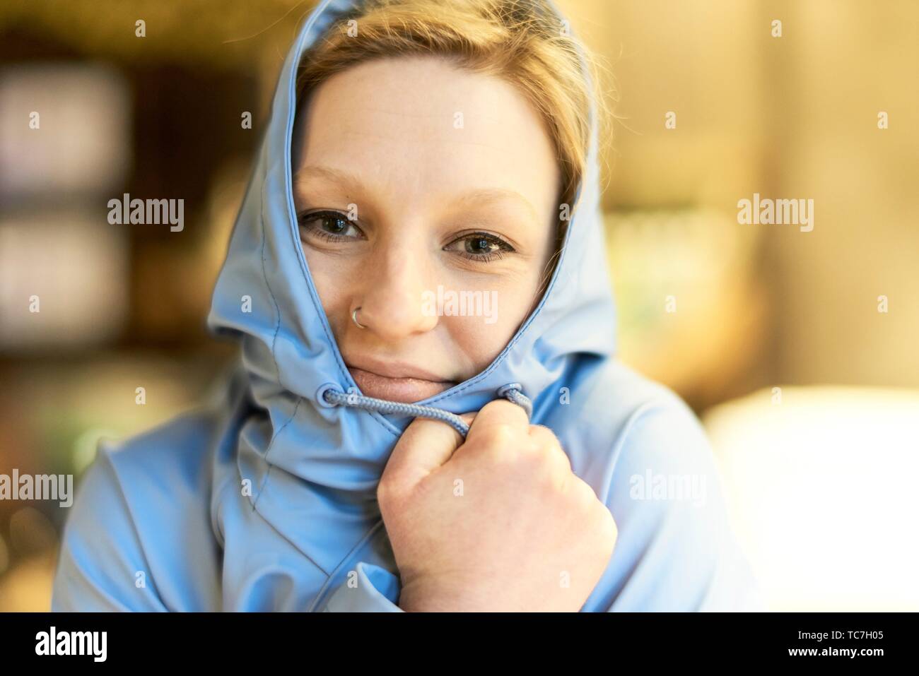Young woman covered in blue rain jacket, in cafe, Munich, Germany Stock