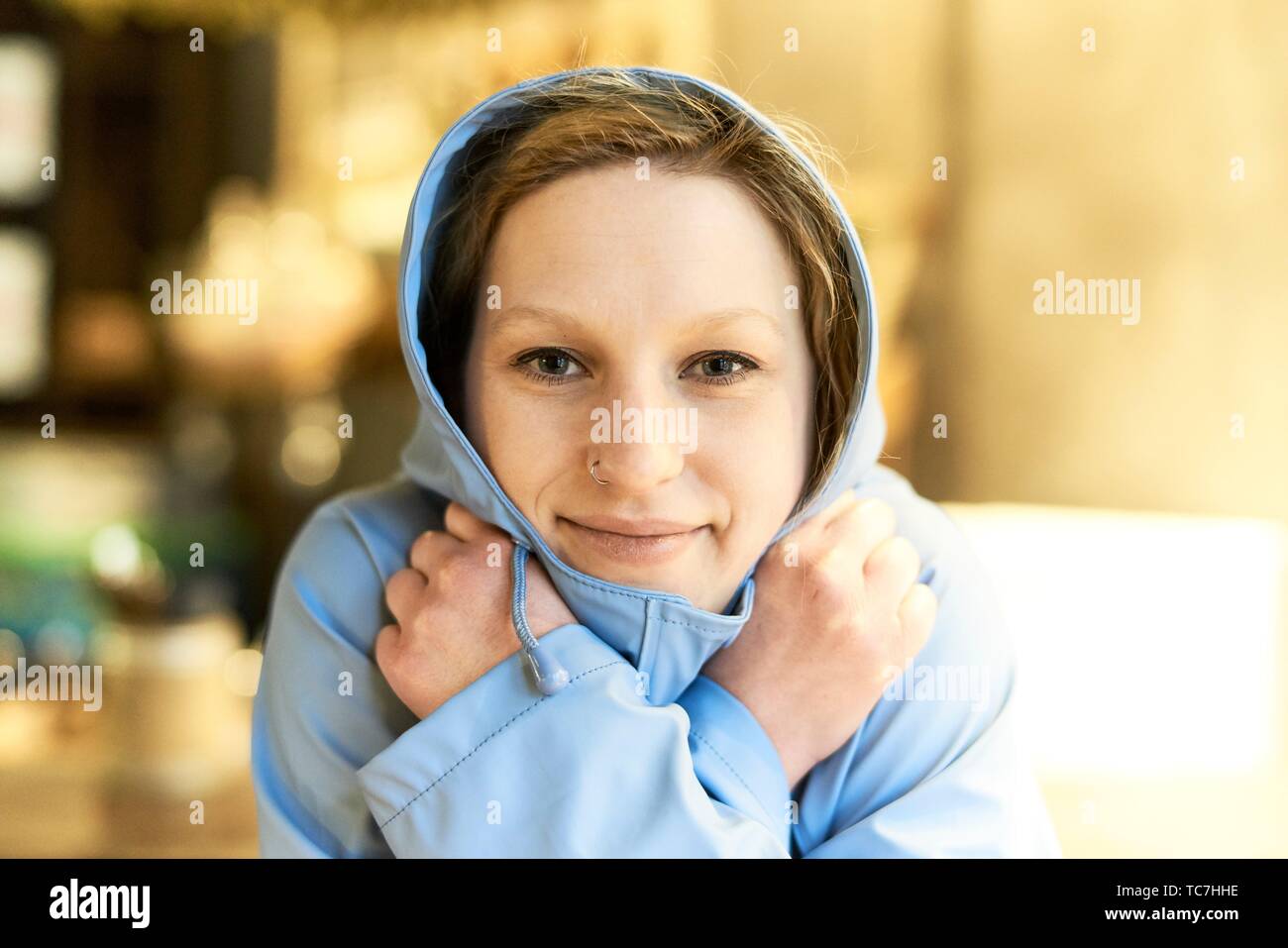 Young woman covered in blue rain jacket, in cafe, Munich, Germany Stock