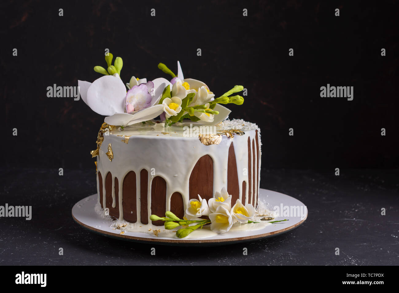 Chocolate cake decorated with flowers and poured white glaze on black stone background. Stock Photo