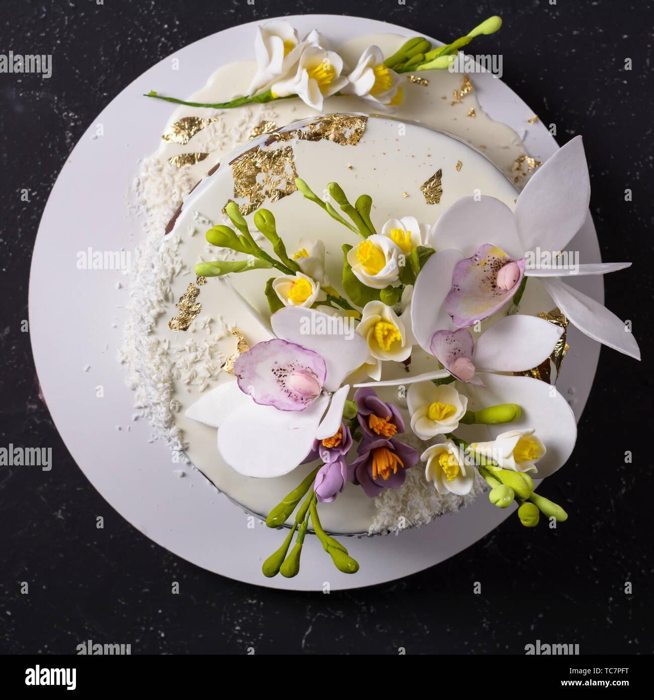 Chocolate cake decorated with flowers and poured white glaze on black stone background. Top view Stock Photo