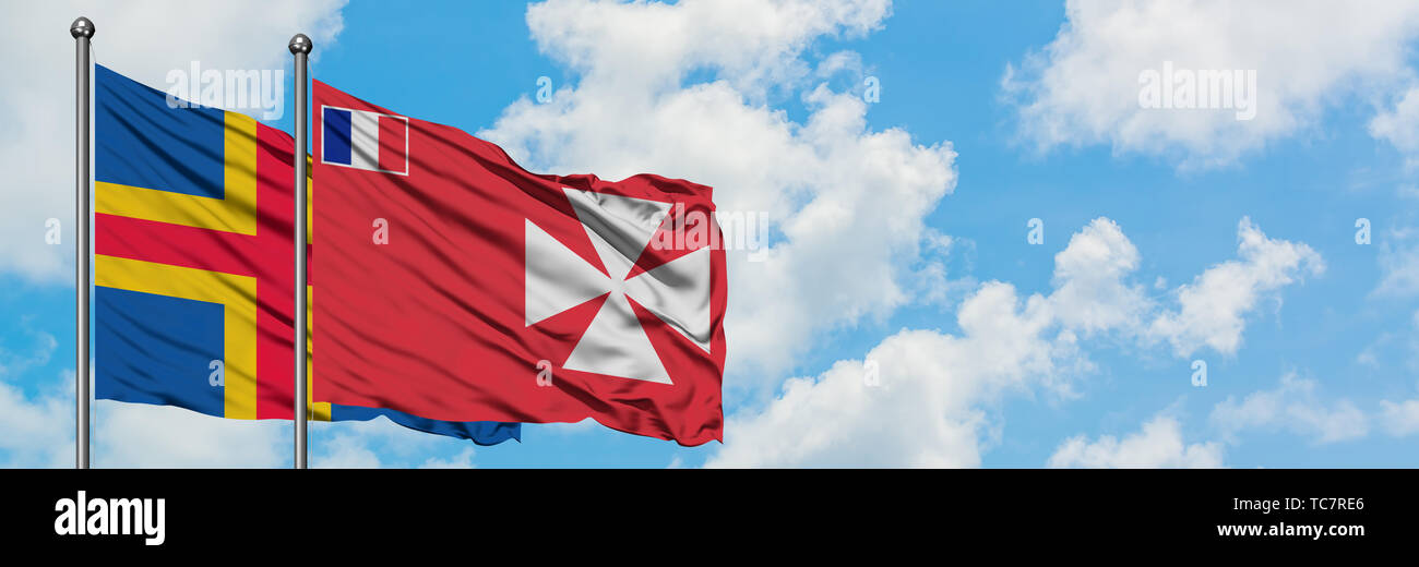 Aland Islands and Wallis And Futuna flag waving in the wind against white cloudy blue sky together. Diplomacy concept, international relations. Stock Photo