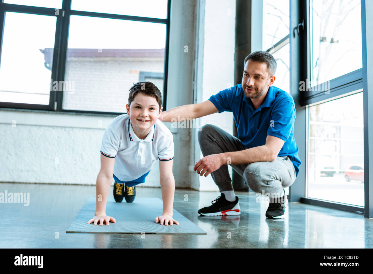 father helping smiling son with plank exercise at gym Stock Photo