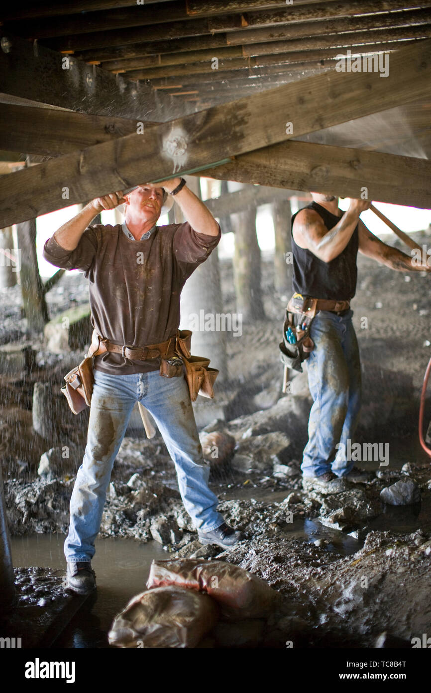 Two male construction workers working underneath a building on a