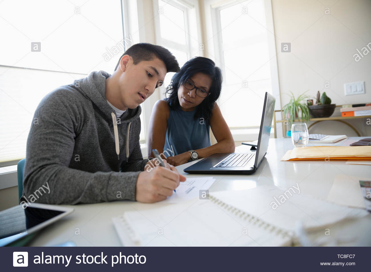Mother helping teenage son fill out college application at table Stock Photo