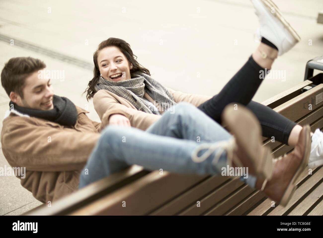 young lively teenage couple sitting on bench the wrong way round in city, hanging out together, legs up, upside down, in Cottbus, Brandenburg, Germany Stock Photo