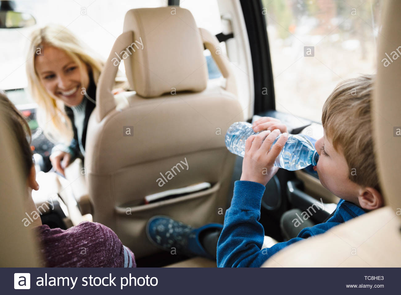 Mother watching thirsty son drinking from water bottle in back seat of SUV Stock Photo
