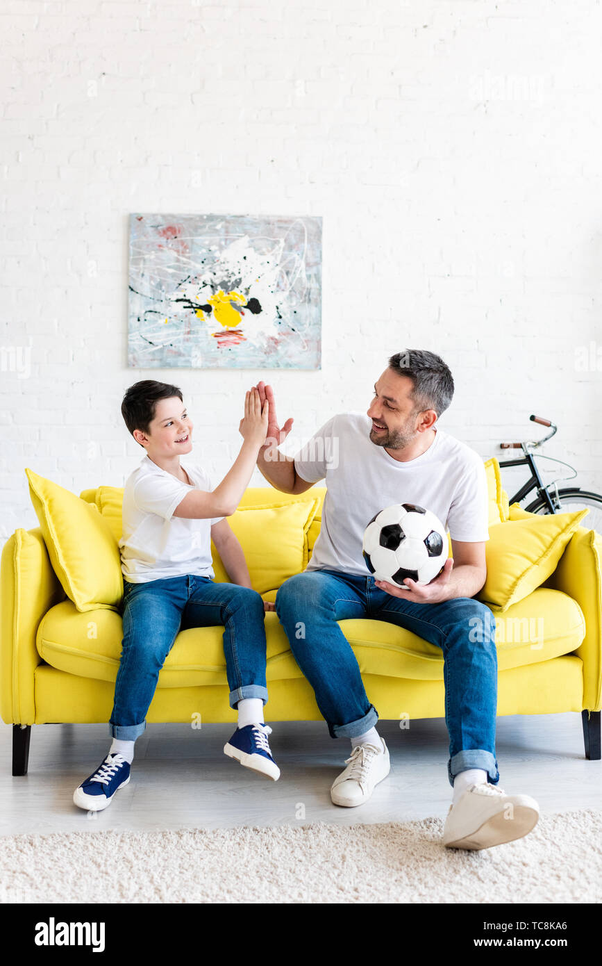 Father And Son Doing High Five Sign While Sitting On Couch With