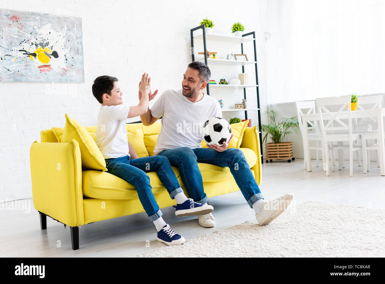 Father And Son Doing High Five Sign While Sitting On Couch With