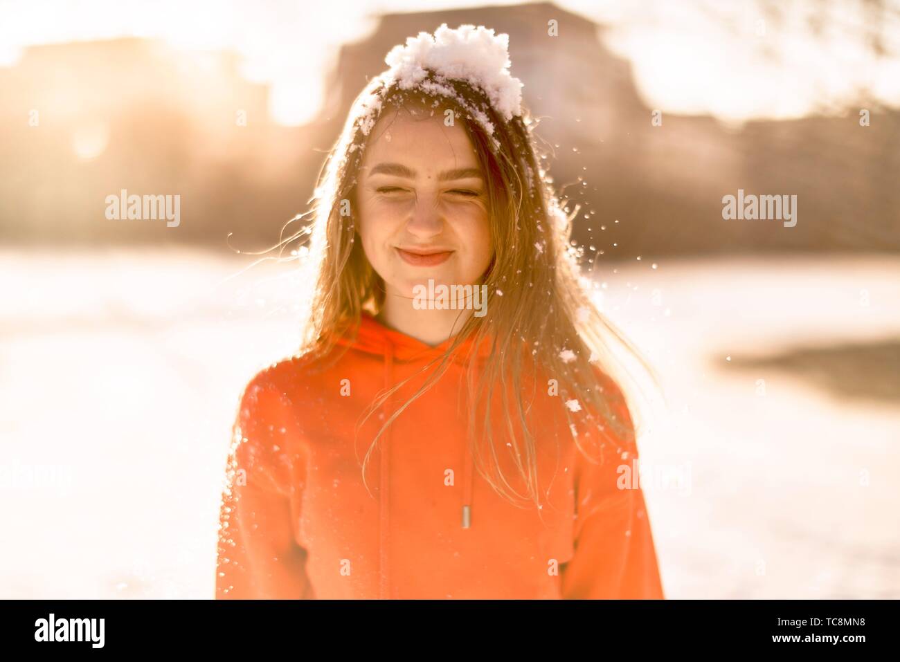 young woman with cold snow on head, squeezing eyes, winter season, wearing orange sweater, in Cottbus, Brandenburg, Germany Stock Photo