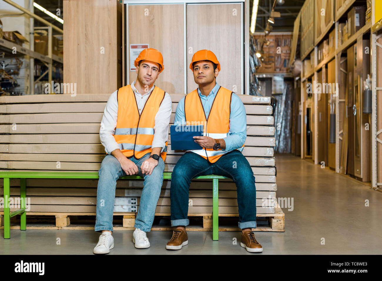 concentrated multicultural workers sitting on bench in warehouse Stock Photo