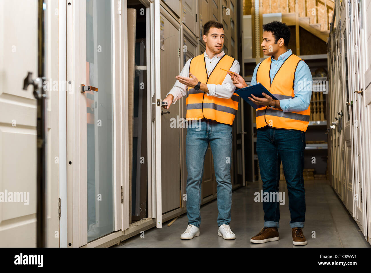 handsome multicultural storehouse workers talking while standing in doors department Stock Photo