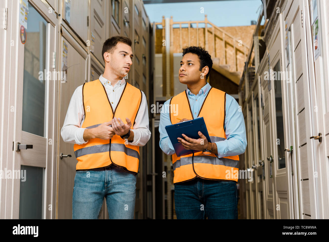 serious multicultural warehouse workers talking while standing in doors department Stock Photo