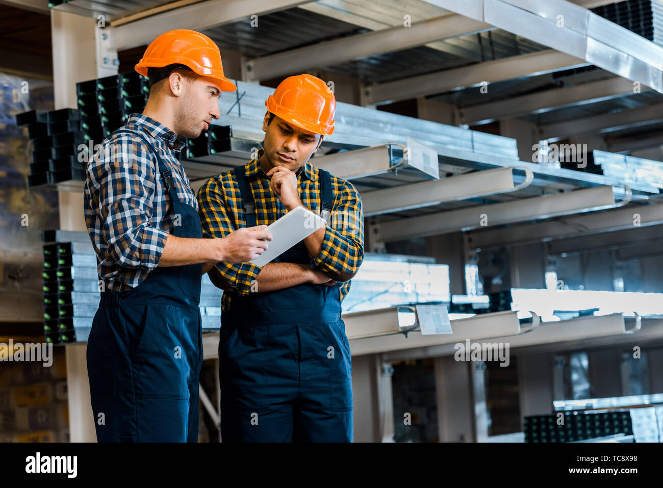 thoughtful multicultural warehouse workers in uniform using digital tablet Stock Photo