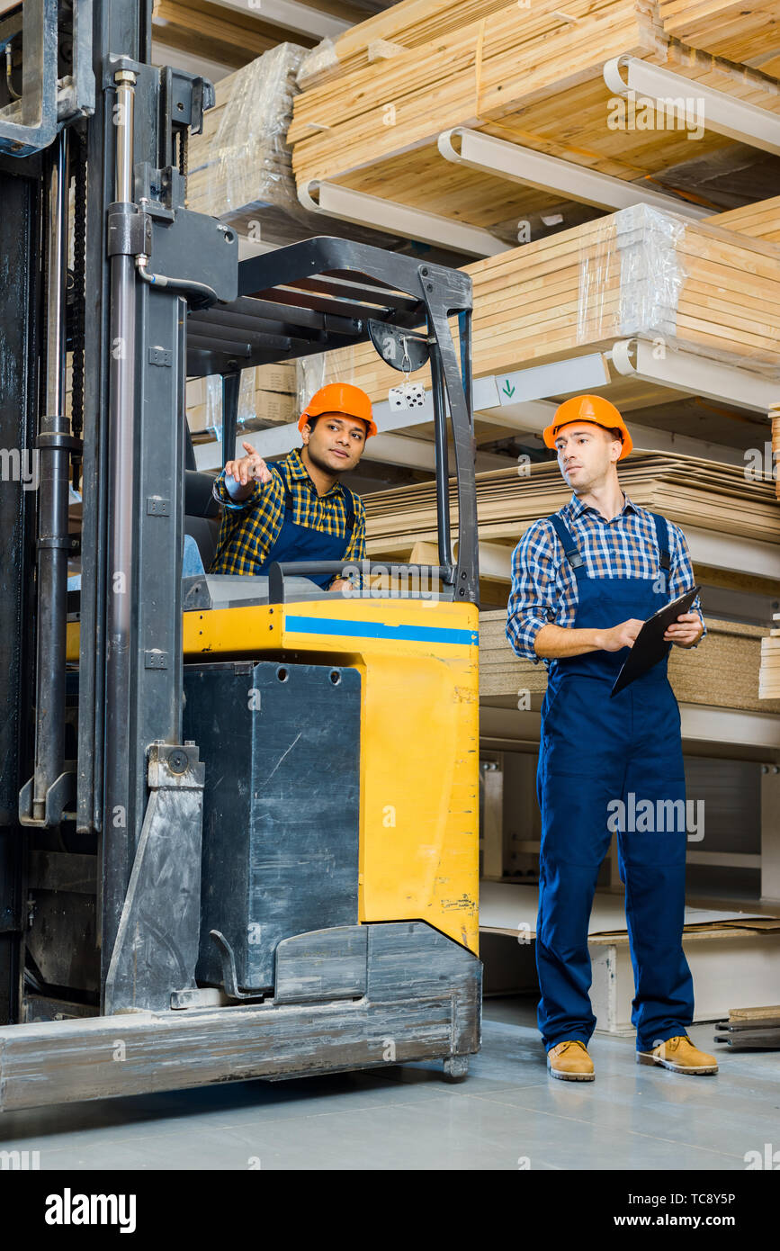 indian worker in forklift machine pointing with finger near colleague