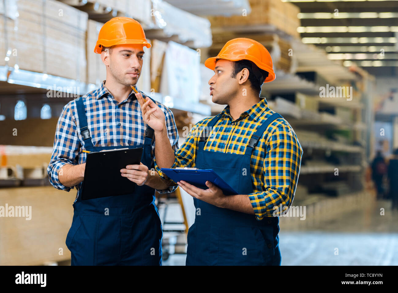 two serious multicultural warehouse workers talking and holding clipboards Stock Photo