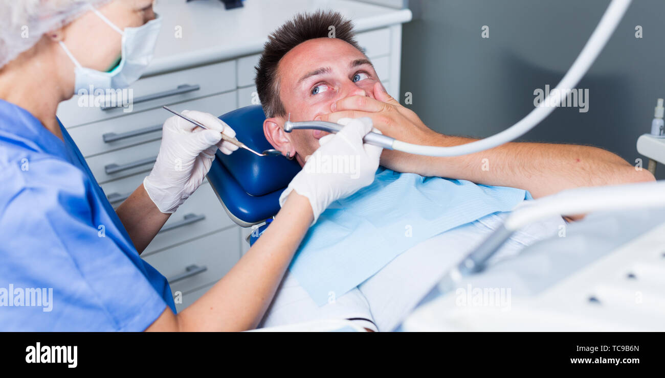 Frightened guy in dental chair not wanting to open his mouth afraid of ...