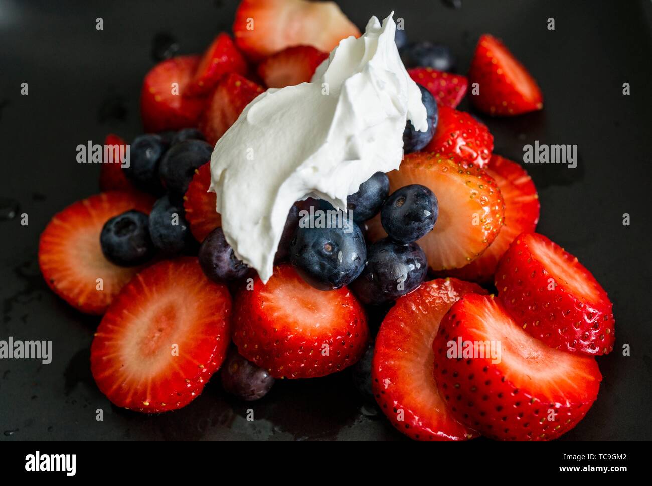 Strawberry slices with blueberries topped with dollop of whipped cream. Macro image against black background. Stock Photo