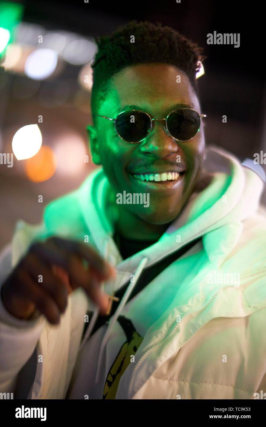 young happy laughing African man in green lights at night, wearing sunglasses, in Munich, Germany Stock Photo