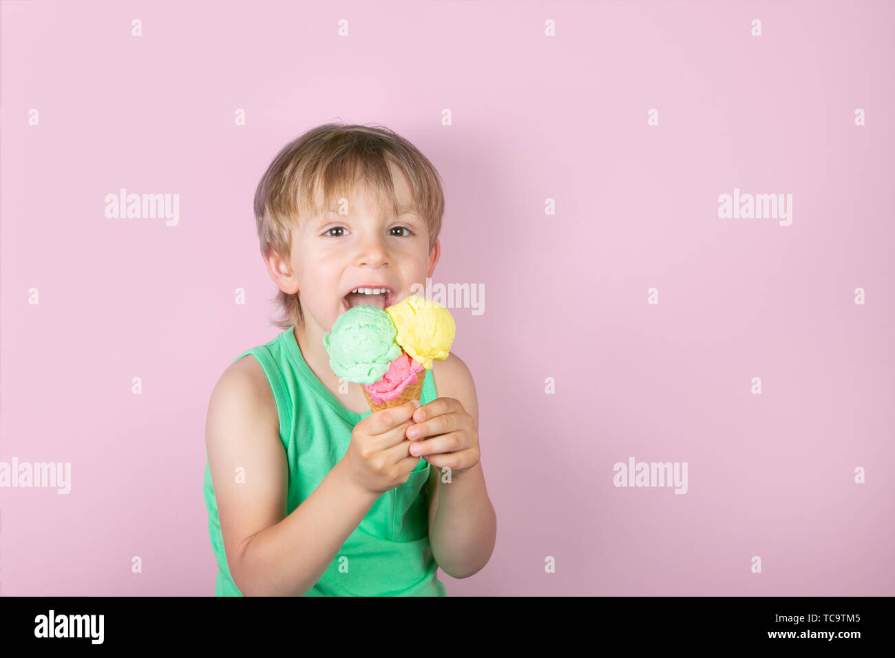 Happy boy eating ice cream in front of pink background Stock Photo