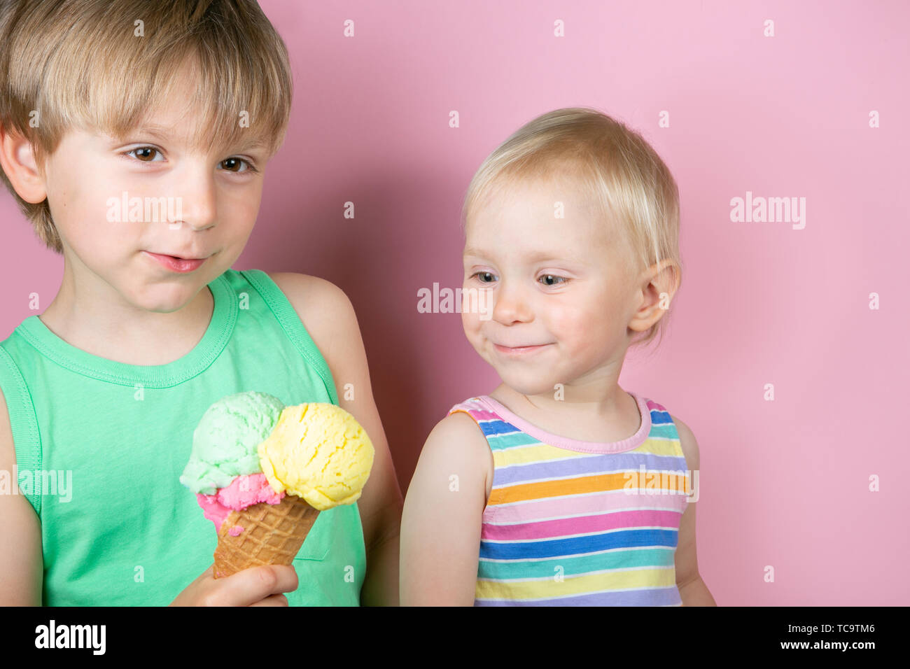 Happy boy and girl eating ice cream in front of pink bakground Stock Photo