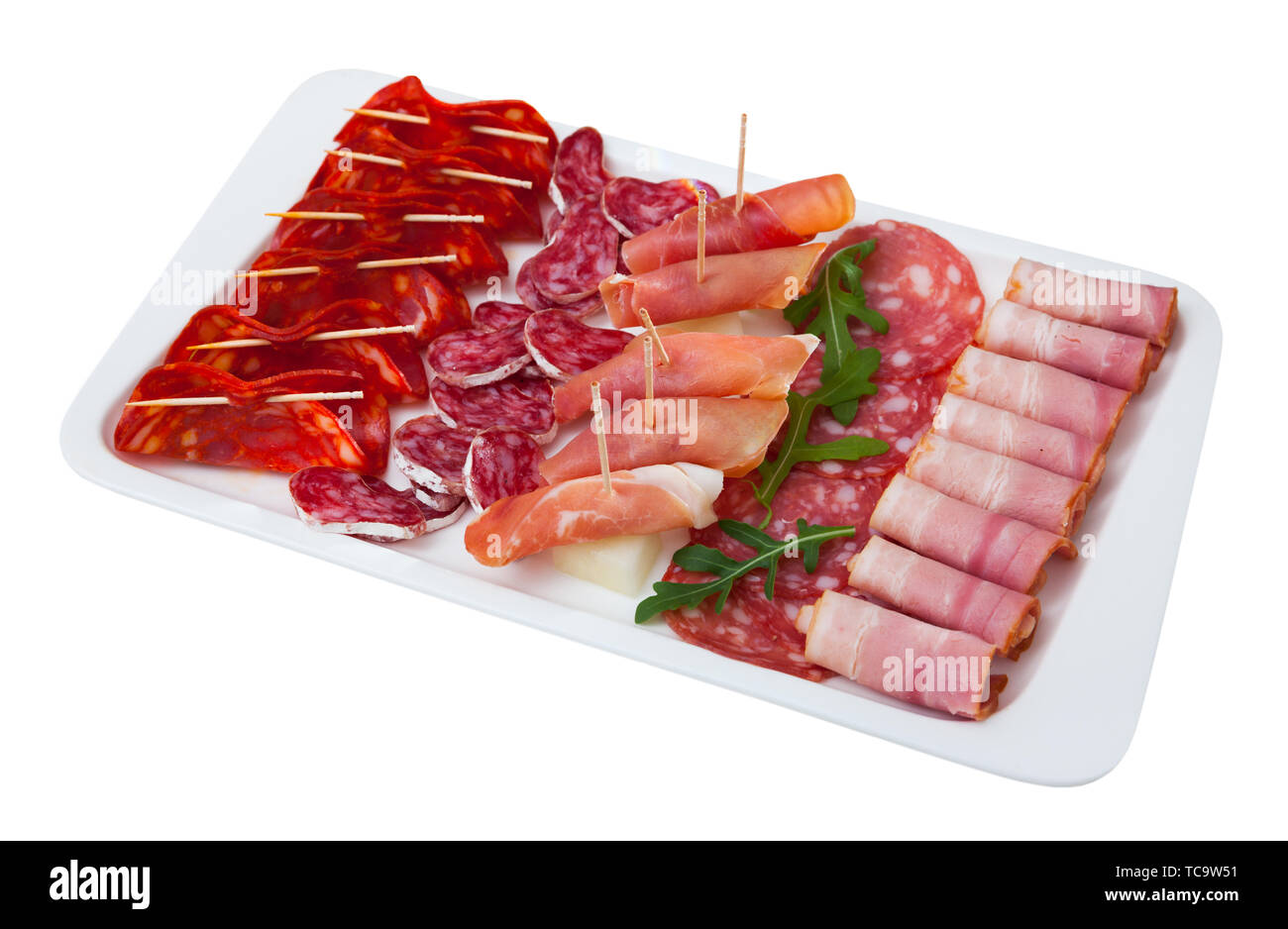 Appetizing cold cuts from Spanish ham, spicy dry-cured sausages and bacon with olives and arugula on white plate. Isolated over white background Stock Photo