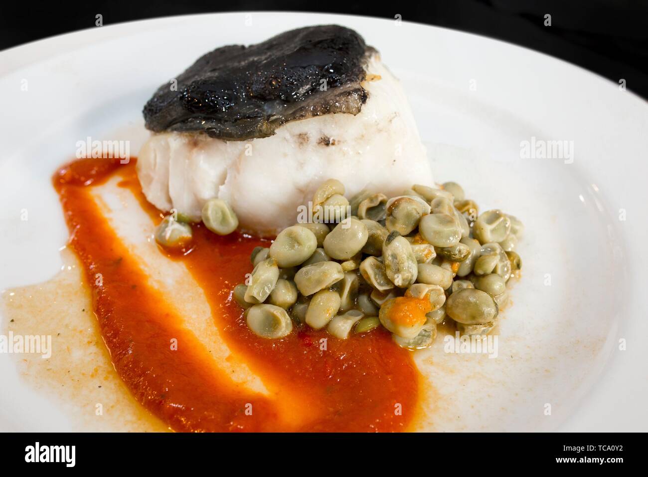 Confit of Cod Fillet, over Tomato Jam and Ali Oli of Black Garlic with sautéed baby greens. Closeup. Stock Photo