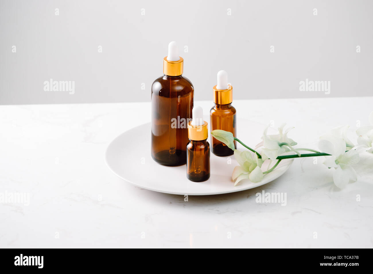 Dropper bottle of organic orchid pure oil on a white surface with orchid heads in the background. Stock Photo