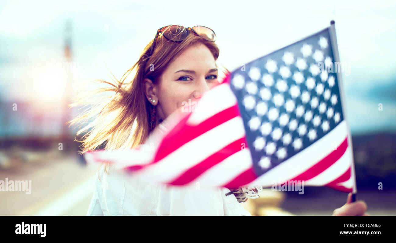 Happy young patriot modern urban woman holding USA flag portrait, depth of field, selective focus Stock Photo