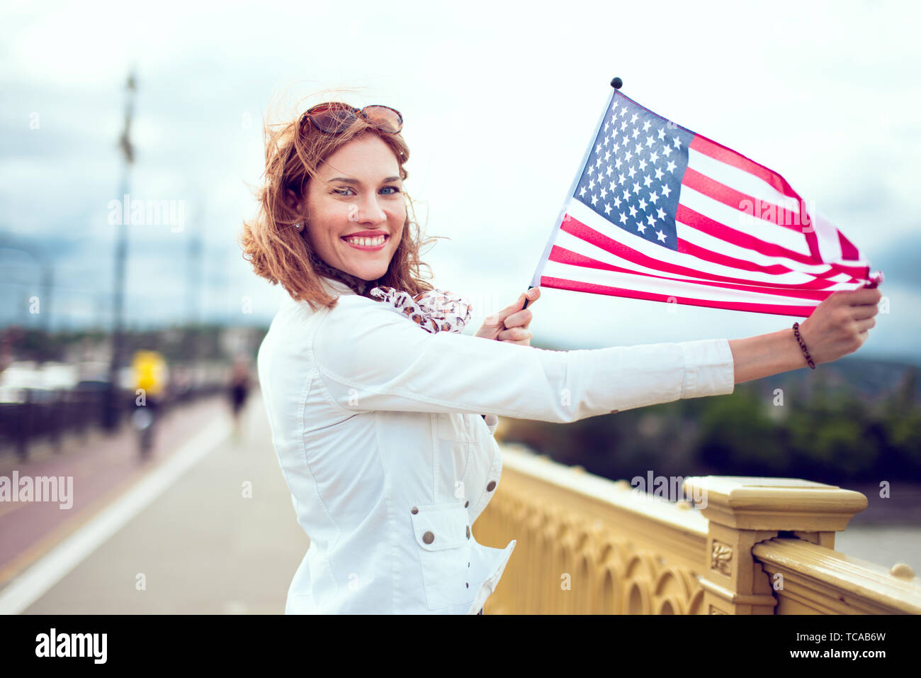 Happy young patriot urban woman with toothy smile enjoying stretching USA flag Stock Photo